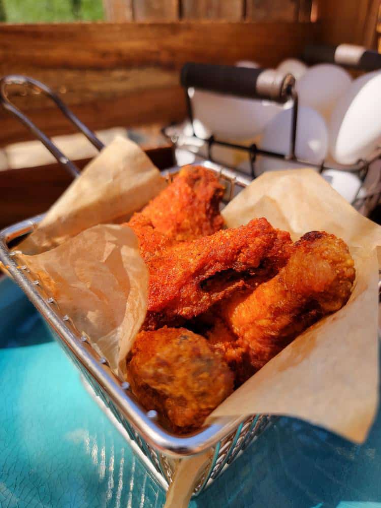 Red chicken wings in a parchment lined basket on a blue table.