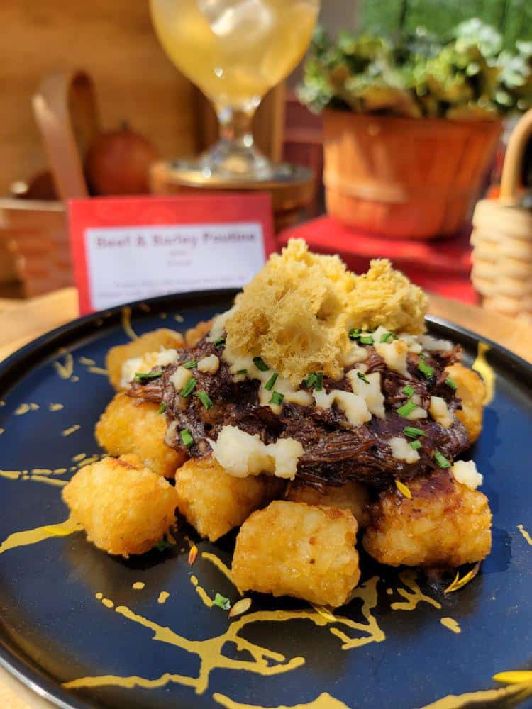 Tater tots topped with meat, cheese curds and a fried cauliflower on a black plate.