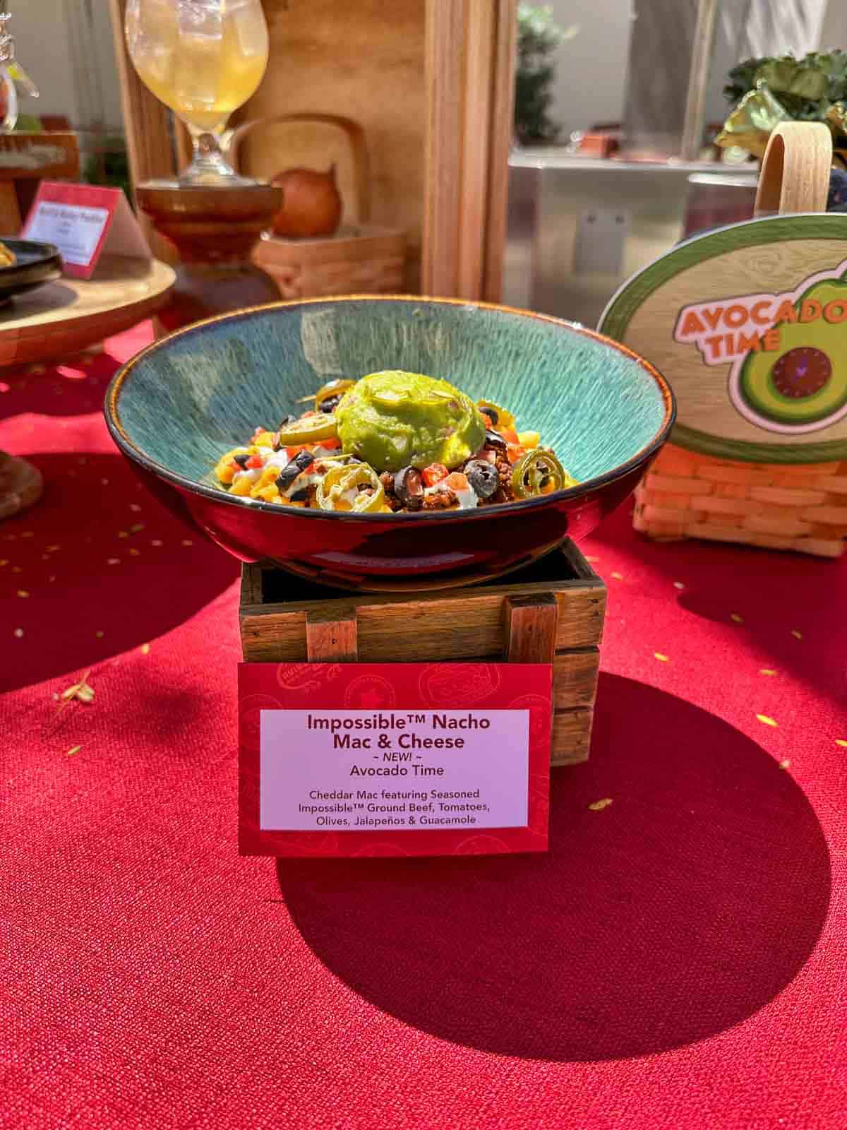 A photo of mac and cheese with taco toppings on top in a turquoise bowl on a wooden stand.