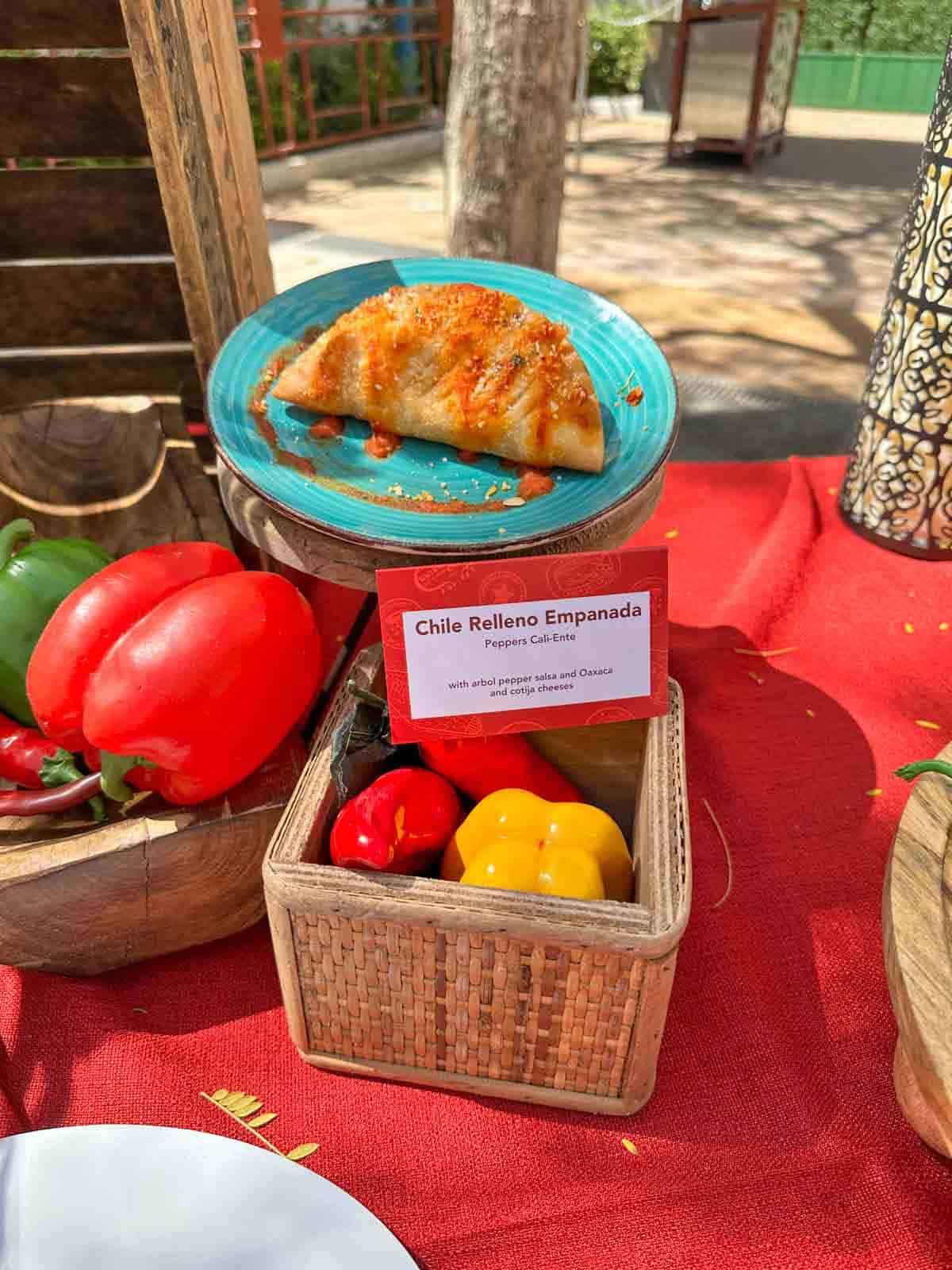 A turquoise plate with an empanada on it sitting above boxes with red and yellow peppers.