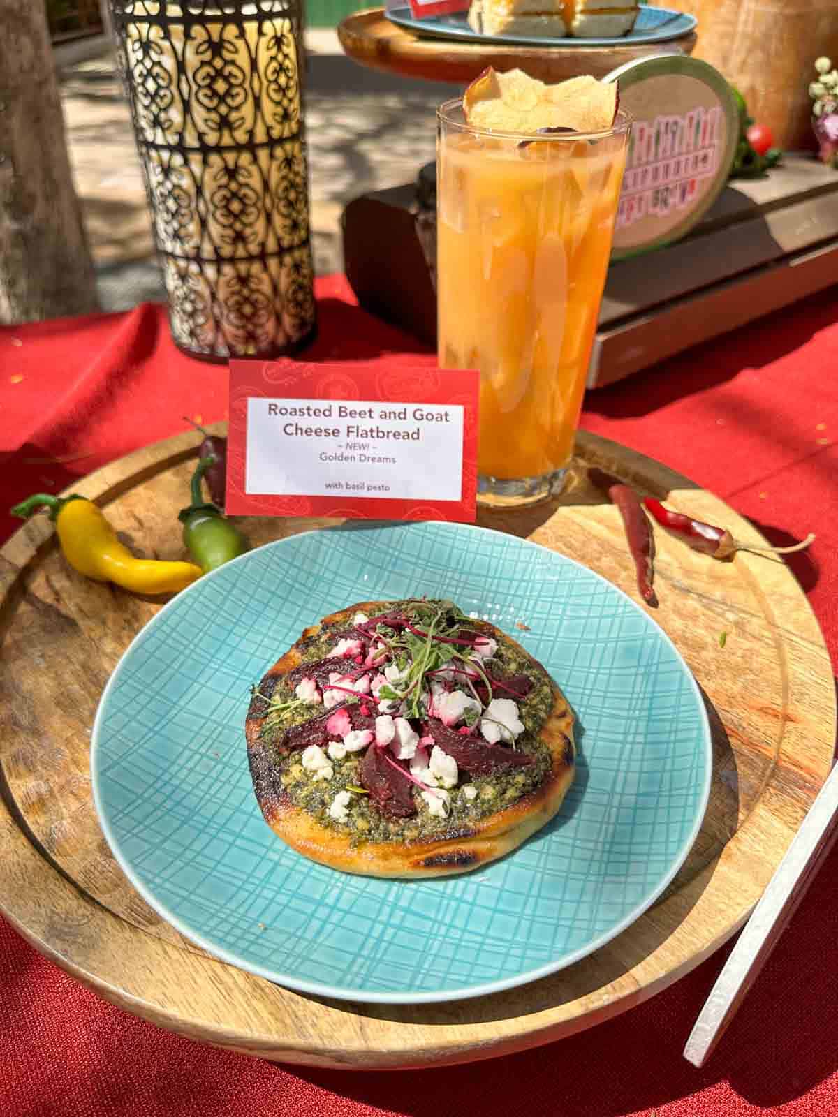 A round flatbread topped with goat cheese and beets sitting on a turquoise plate on a wooden round board.