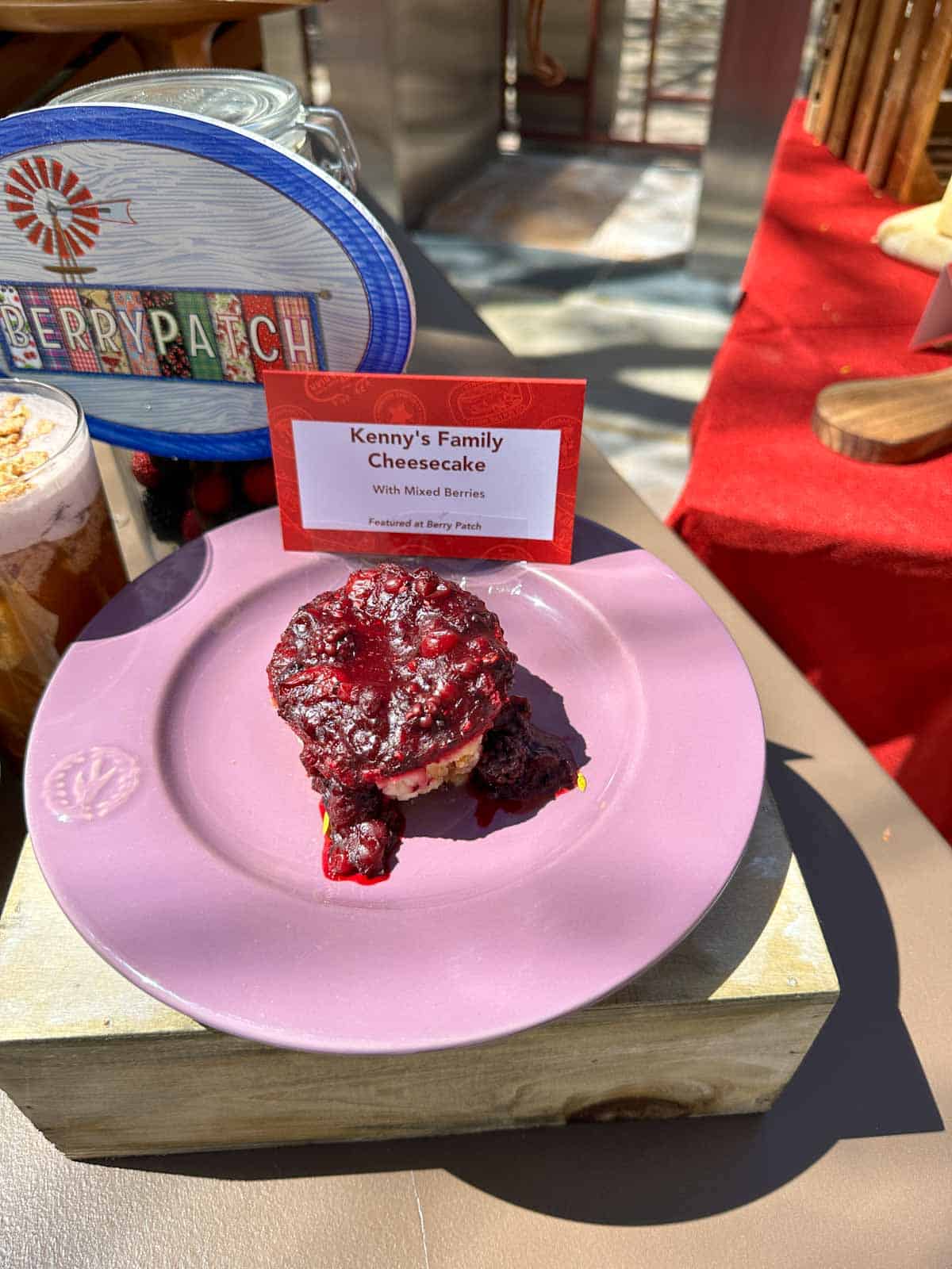 A pink plate with a round piece of cheesecake on it topped with a berry compote.