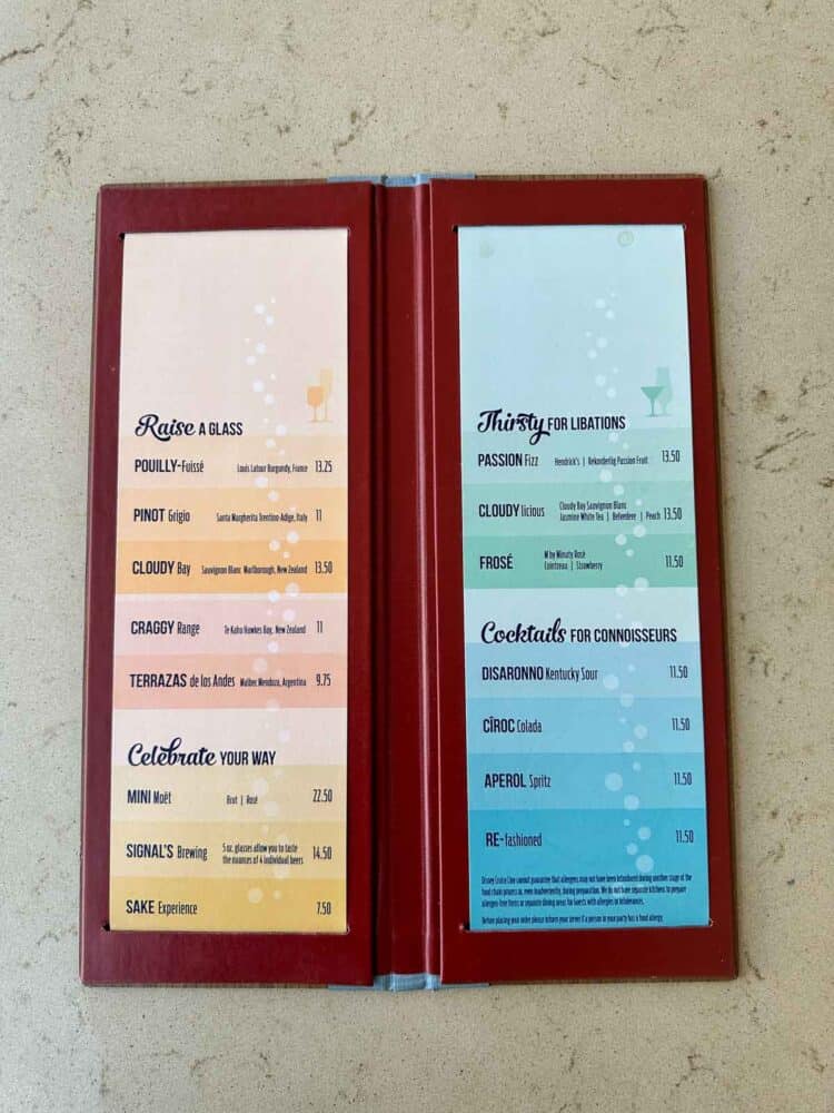 A bar cocktail menu with peach gradient colors on the left and blue on the right opened up on a tan surface.