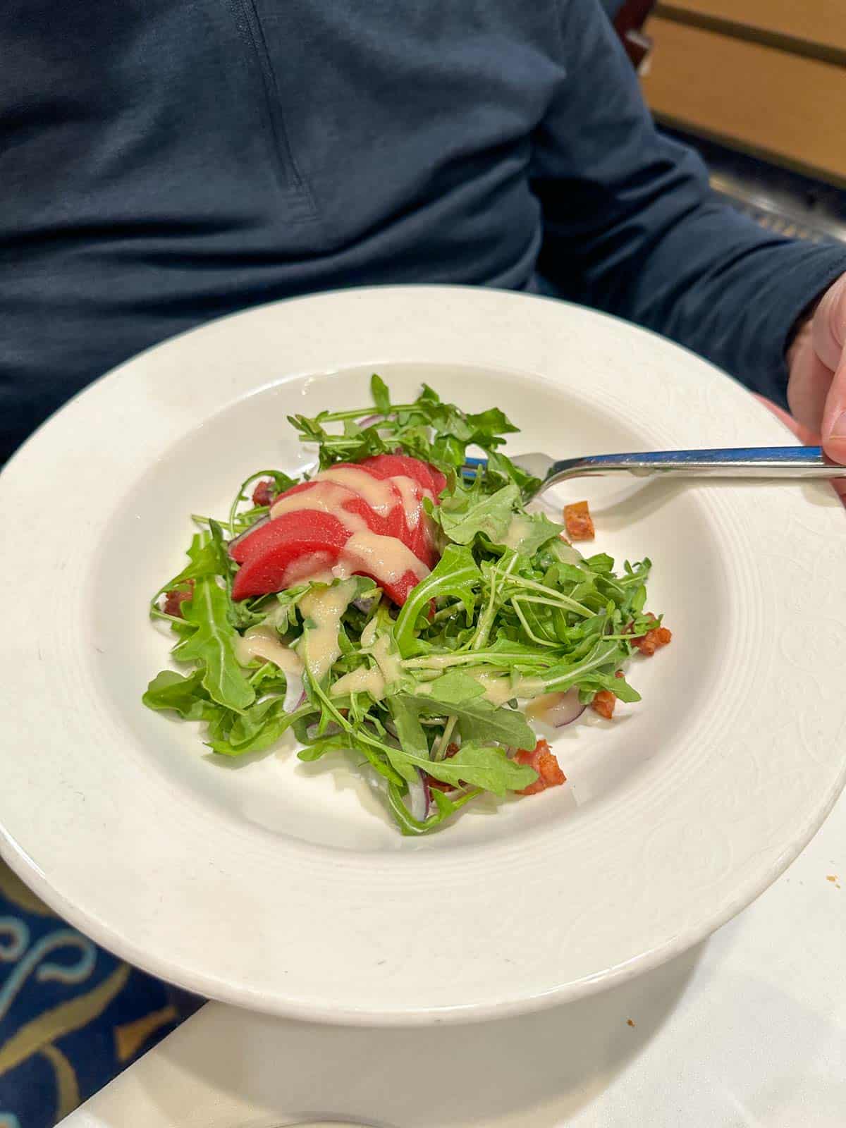A white plate with a green salad topped with radish slices and a whiteish dressing.