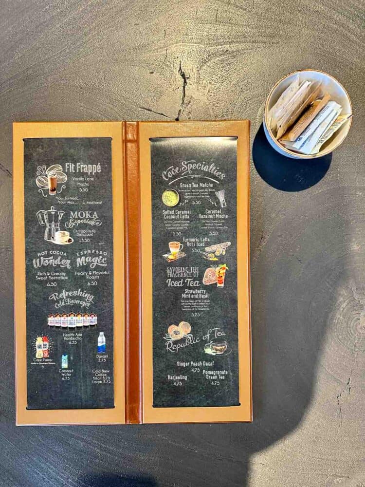 A black cafe menu with a wooden frame sitting on a grey table top.