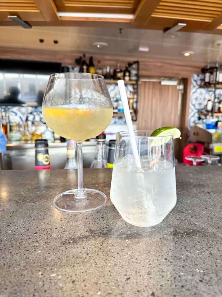 A bar top with a wine glass with yellow liquid and a shorter class with a clear bubbly drink in it.