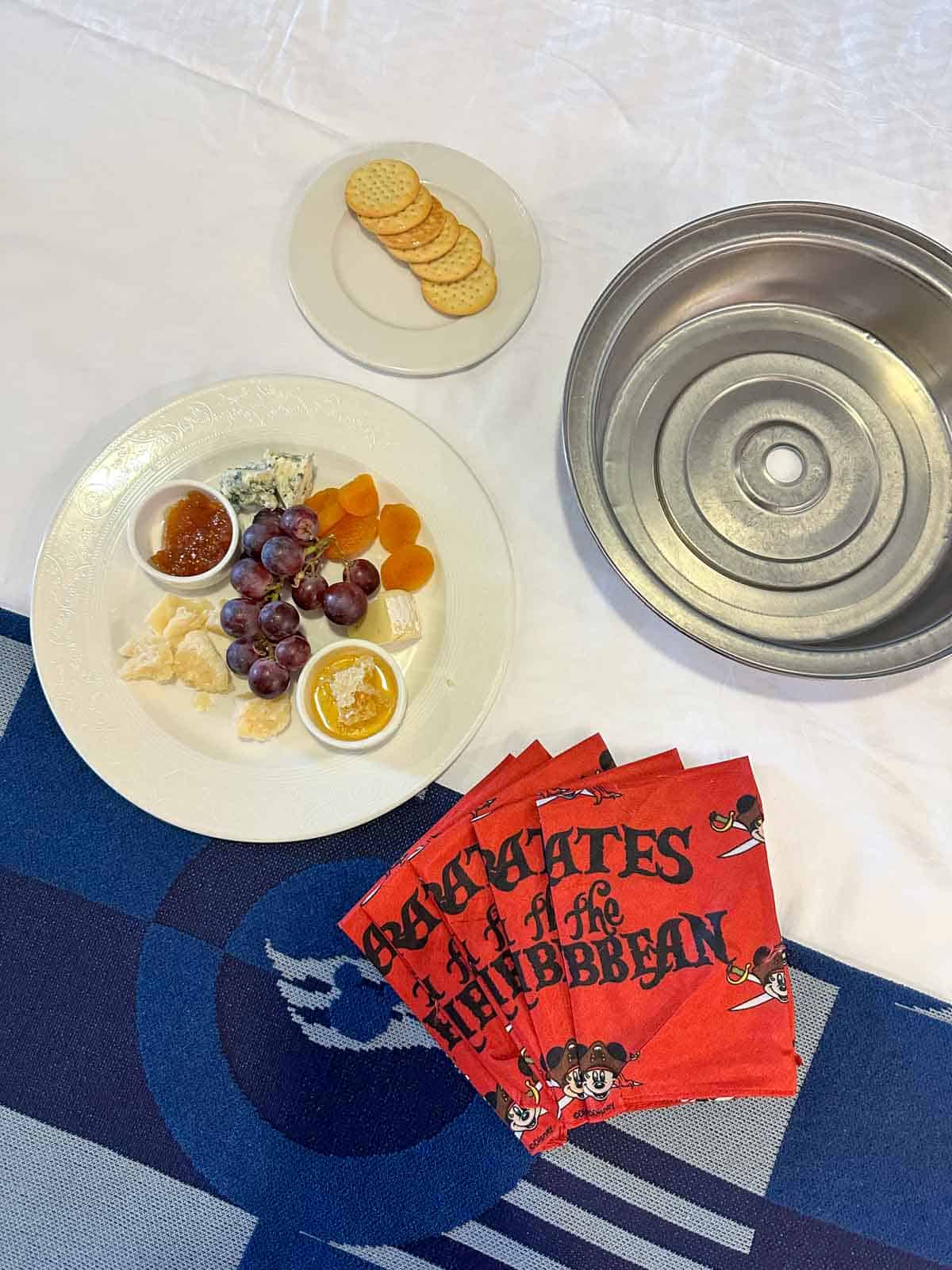 Top view of a blue blanket and white sheets with a plate of cheeses and fruit on top.