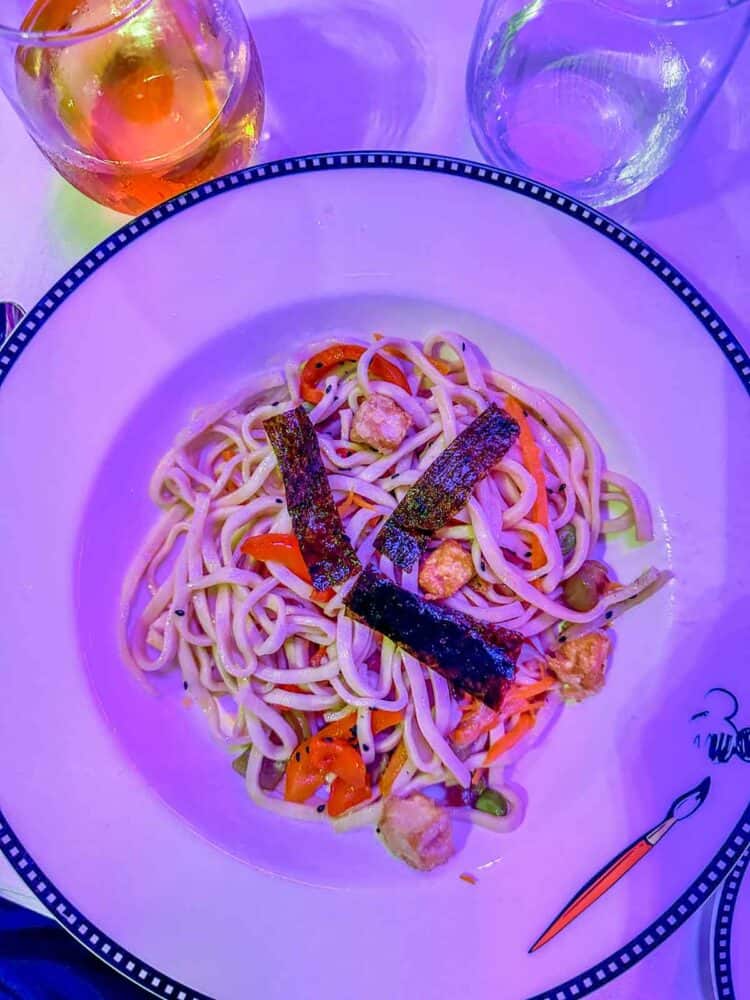 A purple tinted photo of a white plate with spaghetti and veggies in it.