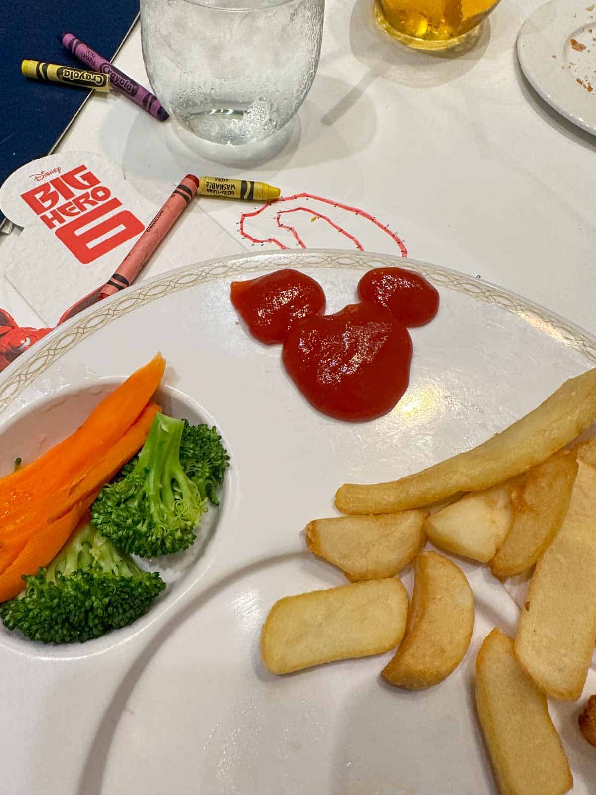A white plate with fries and veggies and a ketchup area shaped like Mickey.