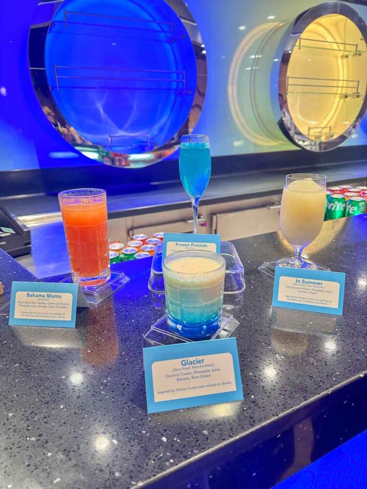 A dark grey counter top with a variety of colorful drinks and signs in front of each one.