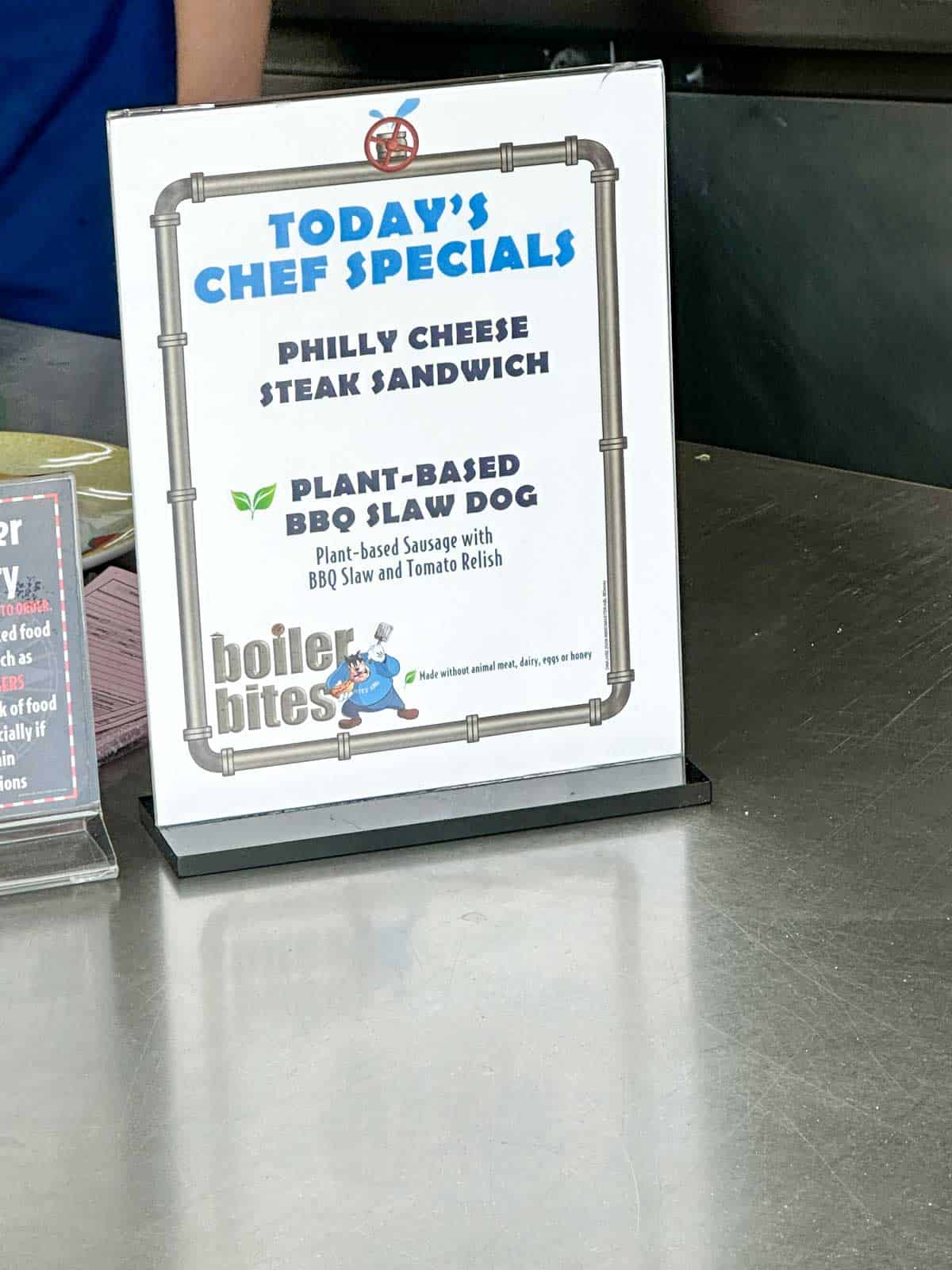 A white sign with blue writing saying today's chef specials and listing a sandwich and hot dog.