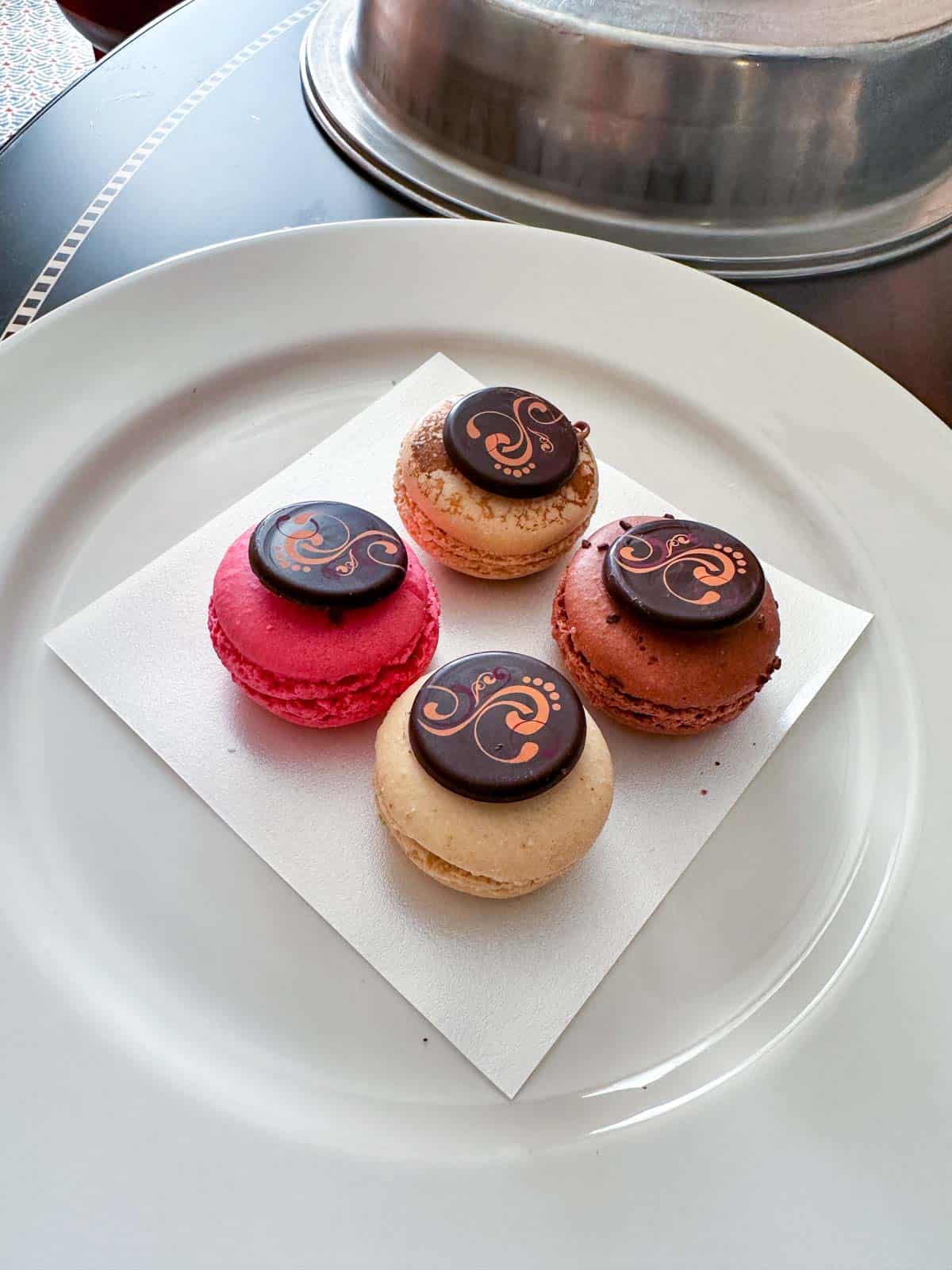 A while plate with four macarons in peach and pink colors and a chocolate circle on top.