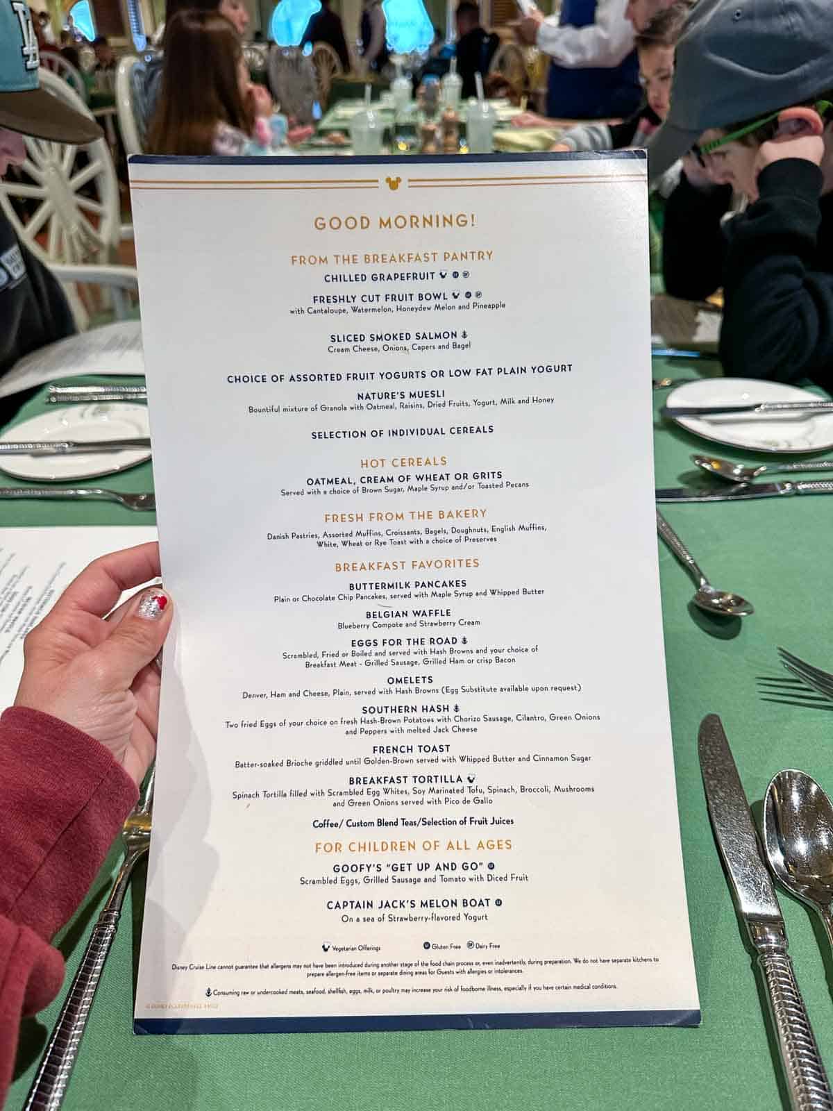 A hand holding a white menu with breakfast items over a green tablecloth.