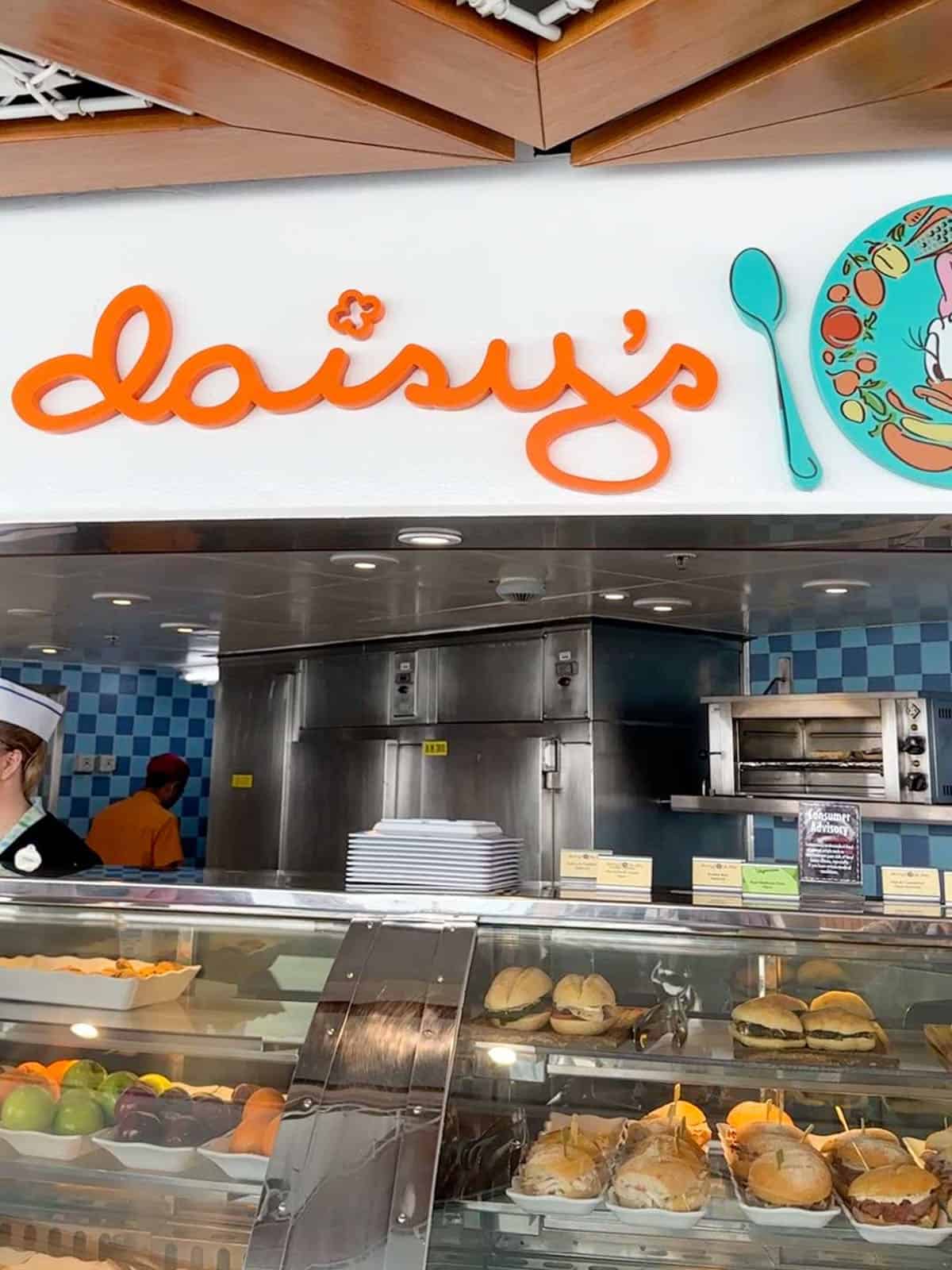 A white sign with orange writing saying Daisy over a sandwich counter service cafe.