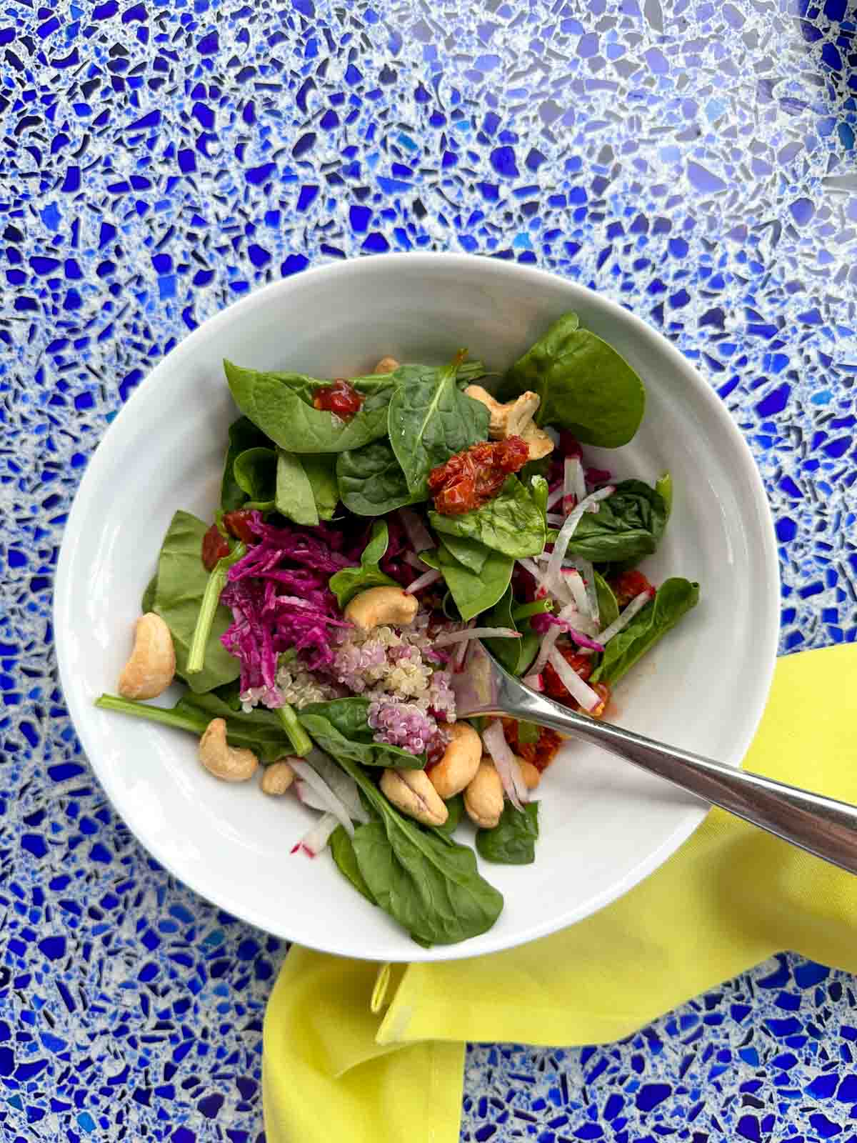 Top view of a white bowl filled with a salad with nuts, veggies and quinoa.