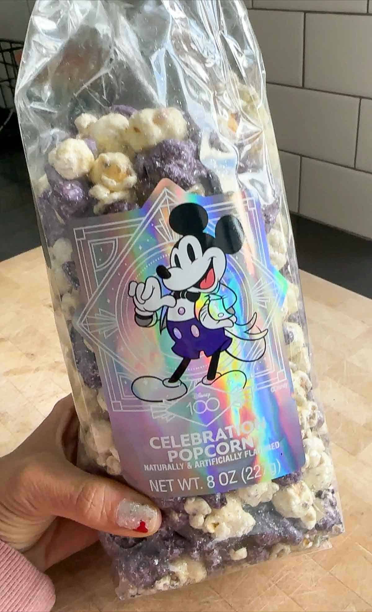 A plastic bag filled with purple and white popcorn and a shiny label with Mickey Mouse on it.