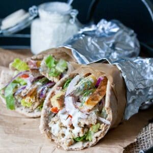 Two gyros with tempeh, onion, tomatoes, tzatziki and potatoes wrapped in foil.