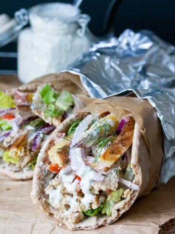 Two gyros with tempeh, onion, tomatoes, tzatziki and potatoes wrapped in foil.
