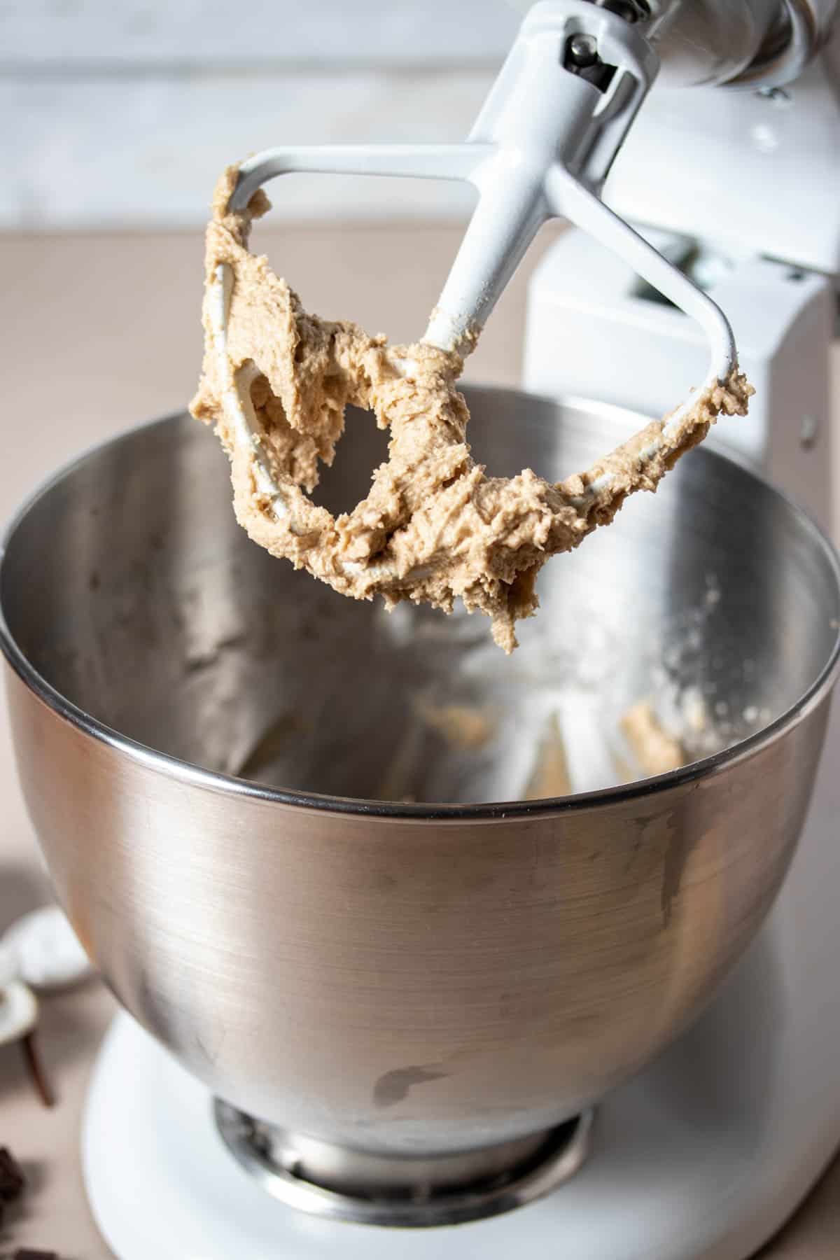 A white stand mixer with a paddle and cookie dough on it without chocolate chips yet.