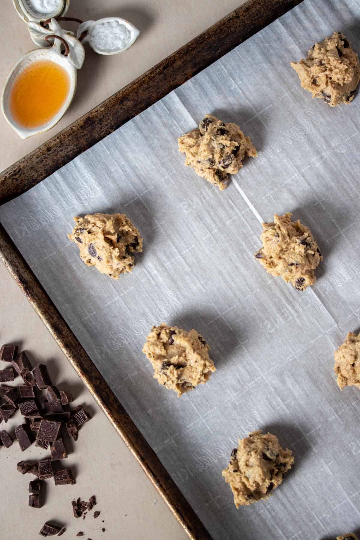 Chocolate chip cookie dough balls on a parchment lined cookie sheet sitting on a tan surface.