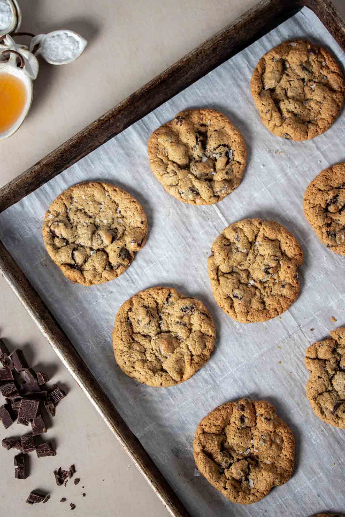 A baking sheet with parchment on it with baked chocolate chip cookies on a tan surface.