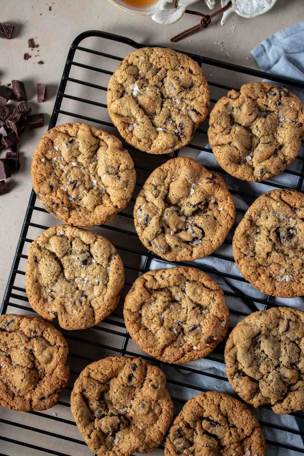 Top view of a black cooling rack on a blue towel lined with rows of chocolate chip cookies sprinkled with salt.