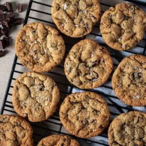 Close up of chocolate chip cookies with salt on top lined up on a black cooling rack.