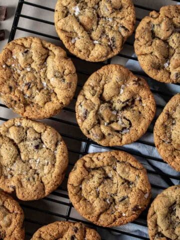 Close up of chocolate chip cookies with salt on top lined up on a black cooling rack.