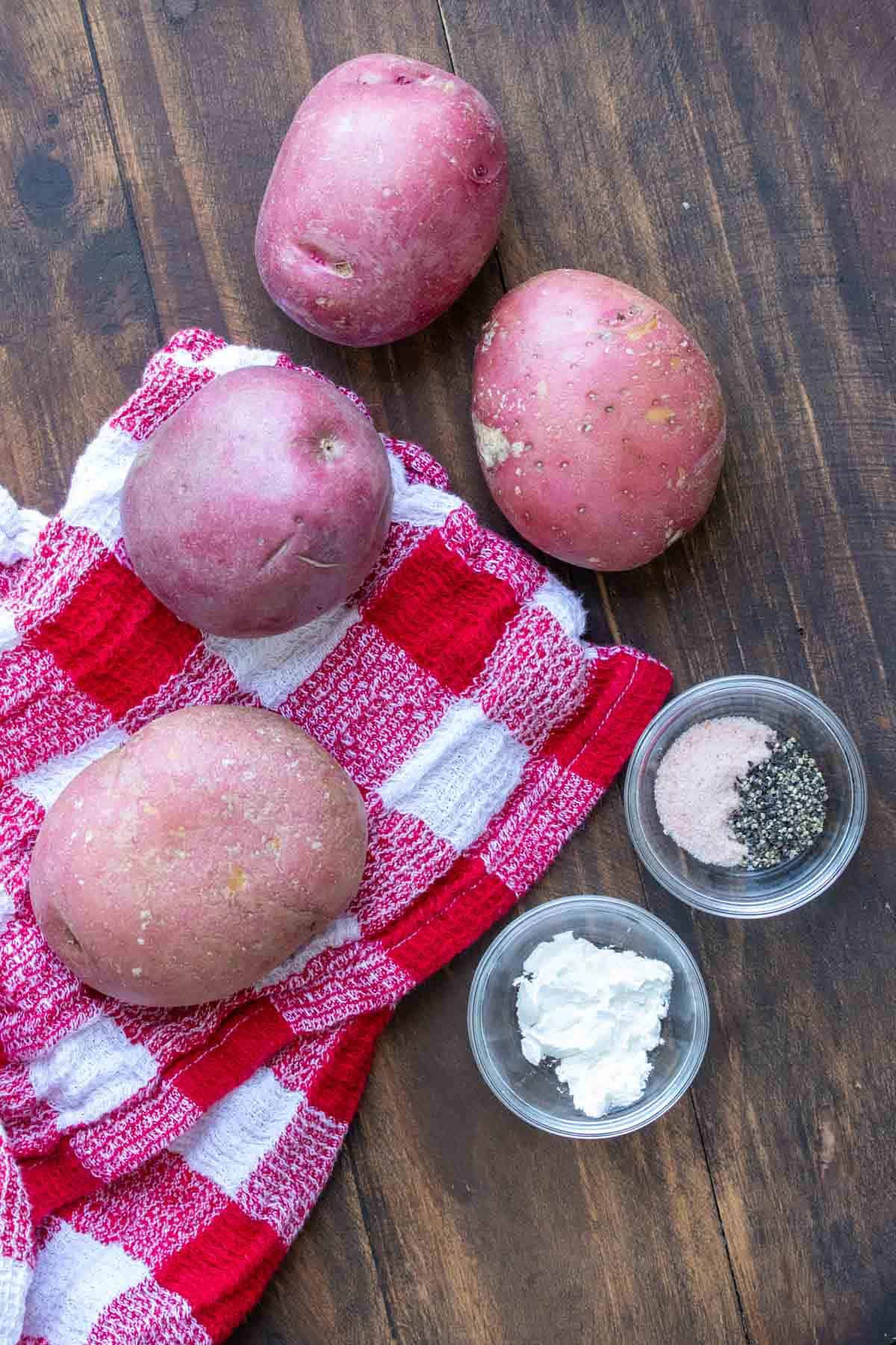 Four red potatoes on a red and white checkered towel next to small bowls of salt and pepper and cornstarch.