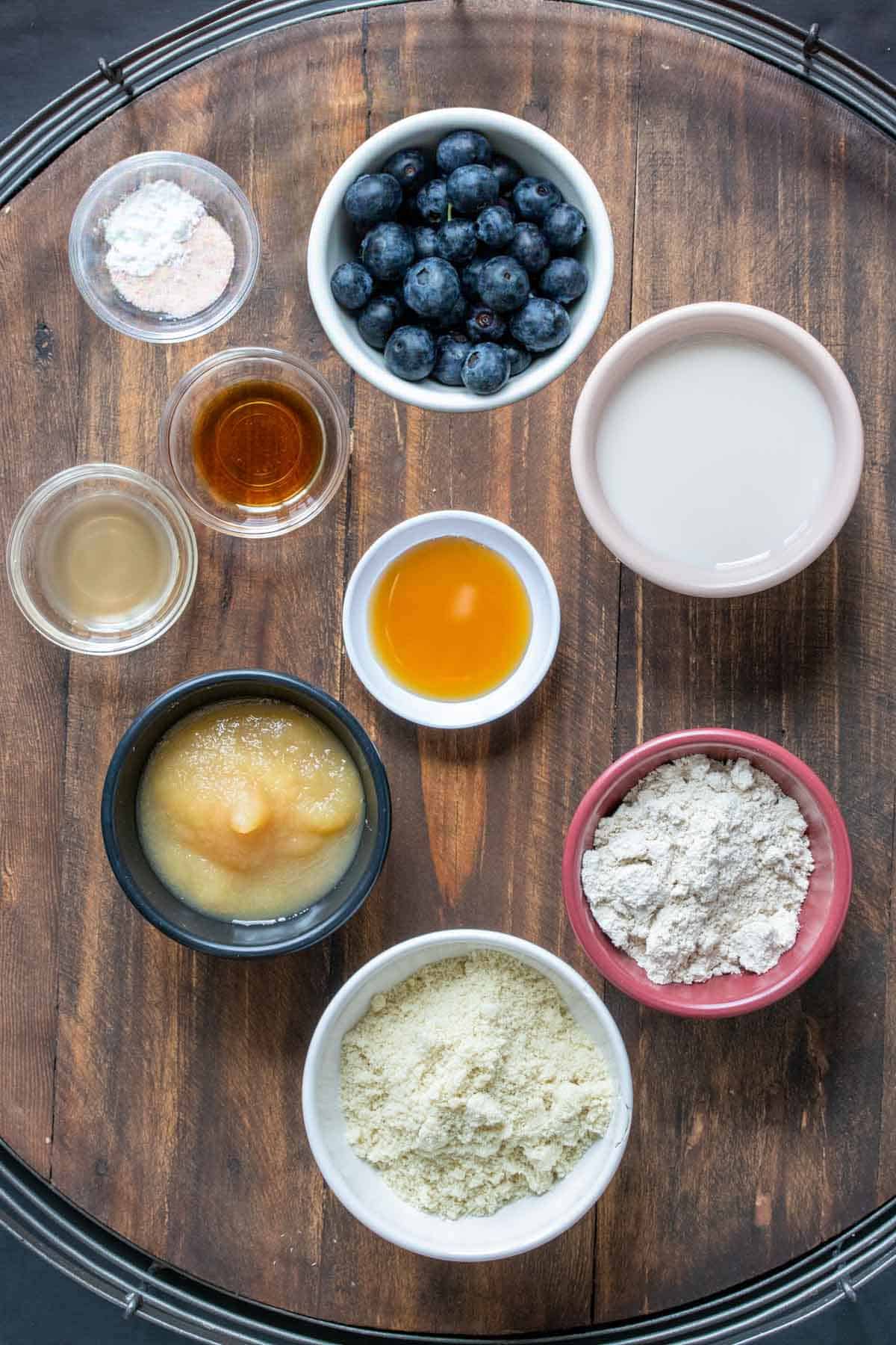 Top view of colorful bowls with ingredients to make blueberry pancakes on a wooden surface.