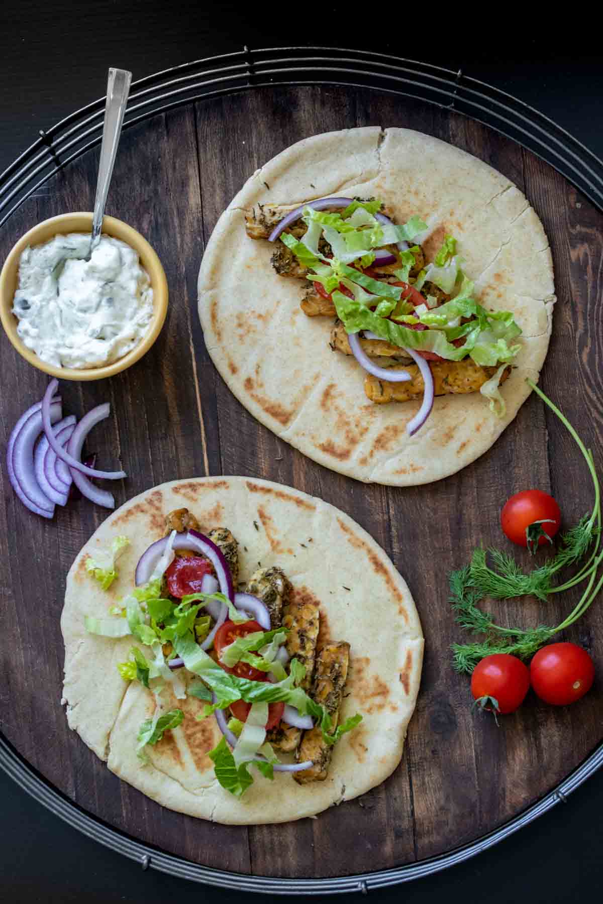 Pita bread slices with tempeh, onion, tomato and lettuce in the center and other gyro ingredients around them.