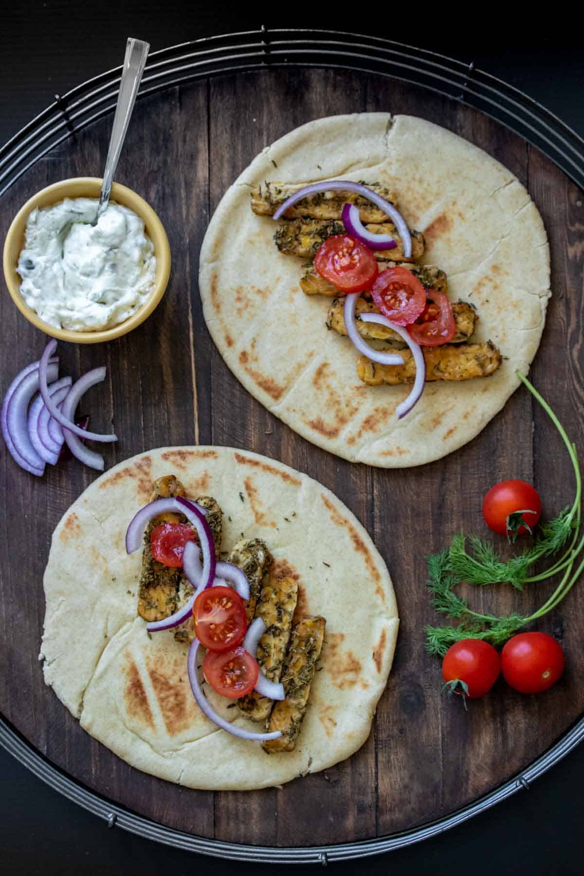 Two pita breads with tempeh, onion and sliced tomatoes and other gyro ingredients next to them.