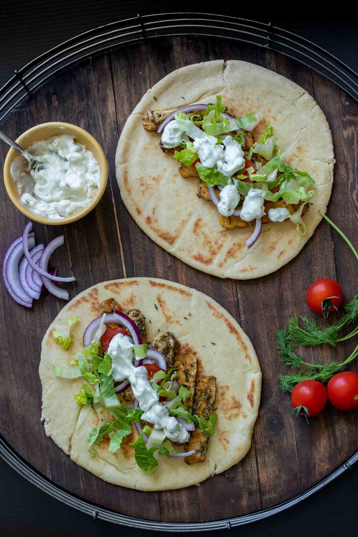 Tempeh gyros open faced on a wooden surface and other gyro ingredients around them.