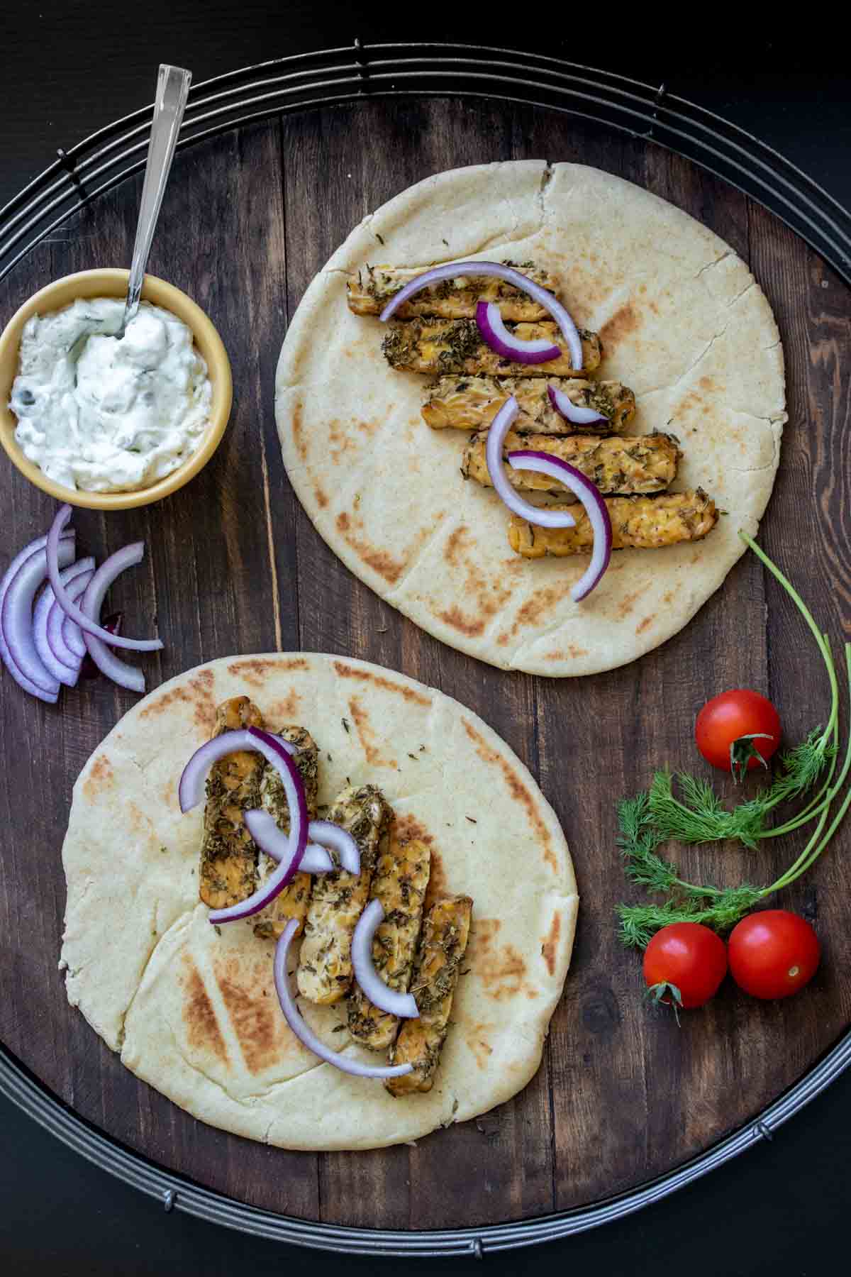 Two pieces of pita bread on a wooden tray with tempeh and red onion in the center.