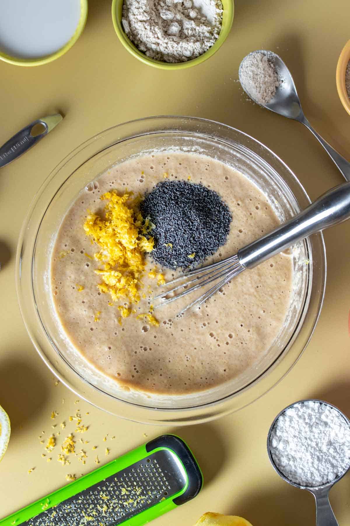 Top view of a glass bowl with batter topped with lemon zest and poppyseeds.