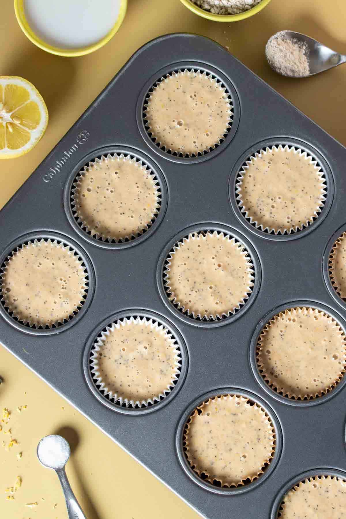 Top view of lemon poppy seed muffin batter in a muffin tin sitting on a yellow surface.