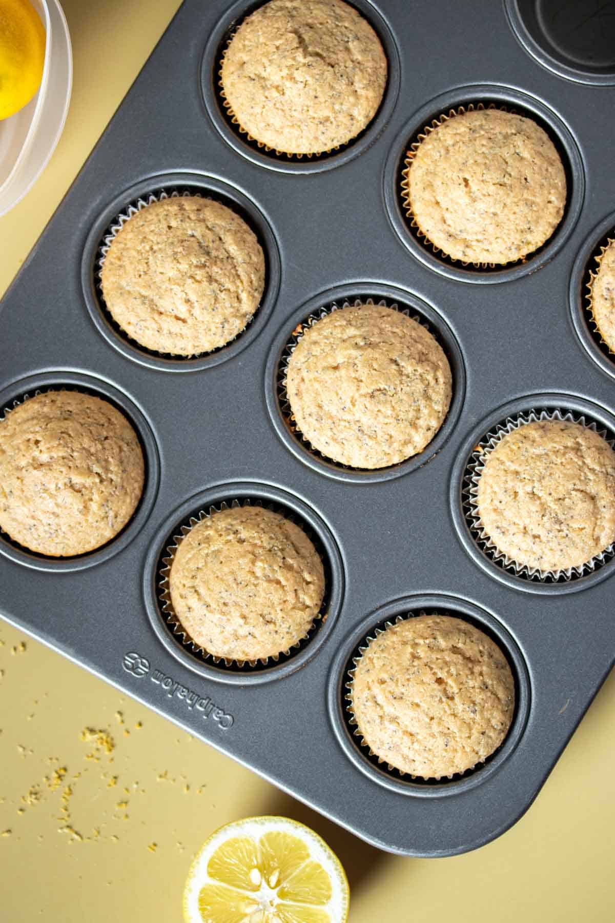 Top view of baked lemon poppy seed muffins in a muffin tin on a yellow surface.