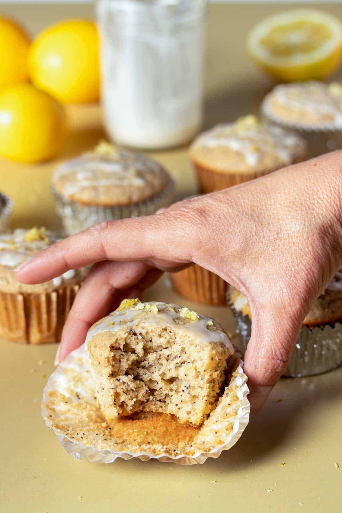 A hand grabbing a lemon poppy seed muffin that has a bite out of it next to other muffins.