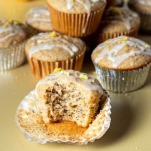 A bite out of a lemon poppy seed muffin sitting in an open muffin liner next to other muffins.