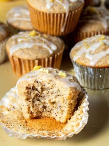 A bite out of a lemon poppy seed muffin sitting in an open muffin liner next to other muffins.