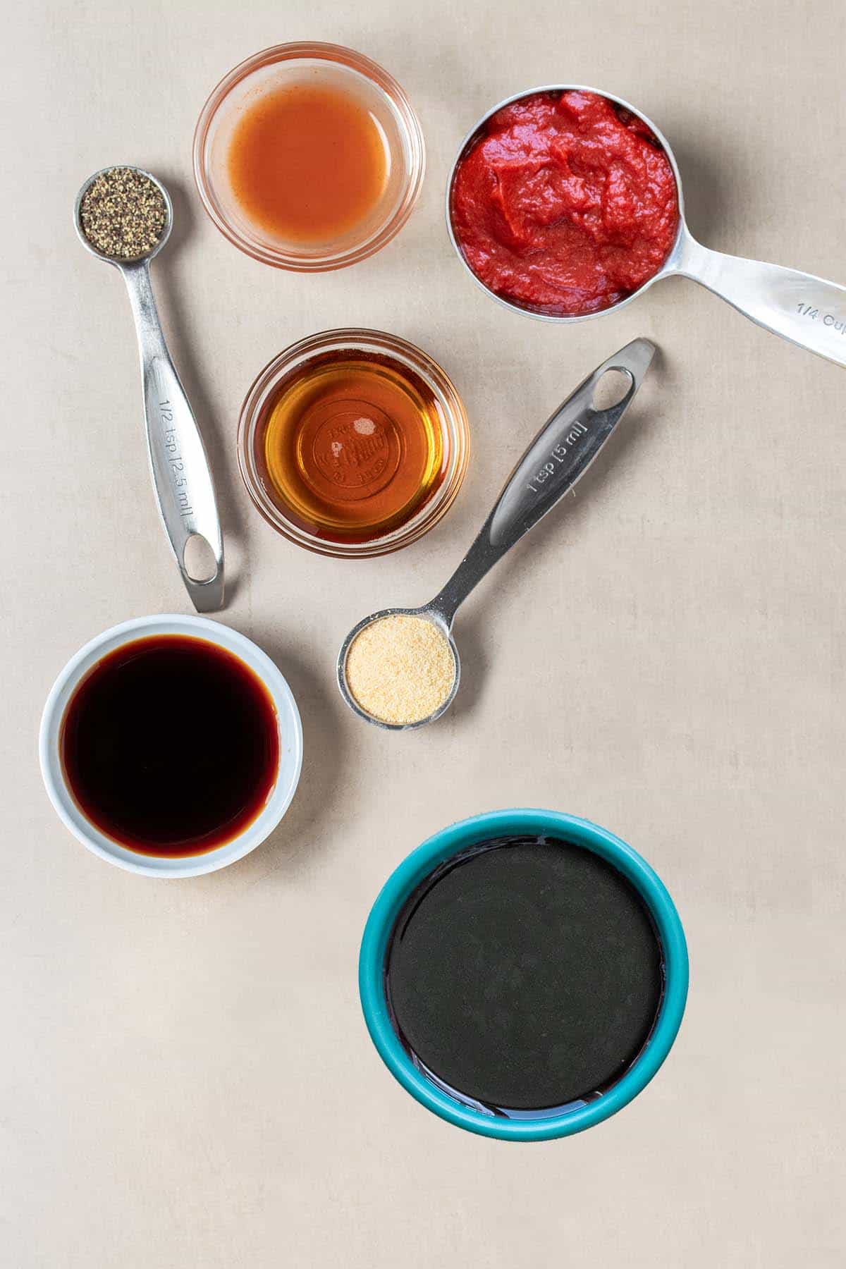 Tan surface with measuring spoons and bowls with ingredients to make a homemade steak sauce.