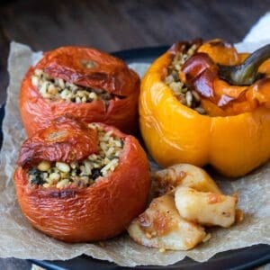 Two tomatoes and one yellow pepper stuffed with a rice mixture and baked on a black plate lined with parchment.