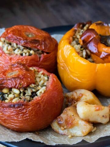 Two tomatoes and one yellow pepper stuffed with a rice mixture and baked on a black plate lined with parchment.