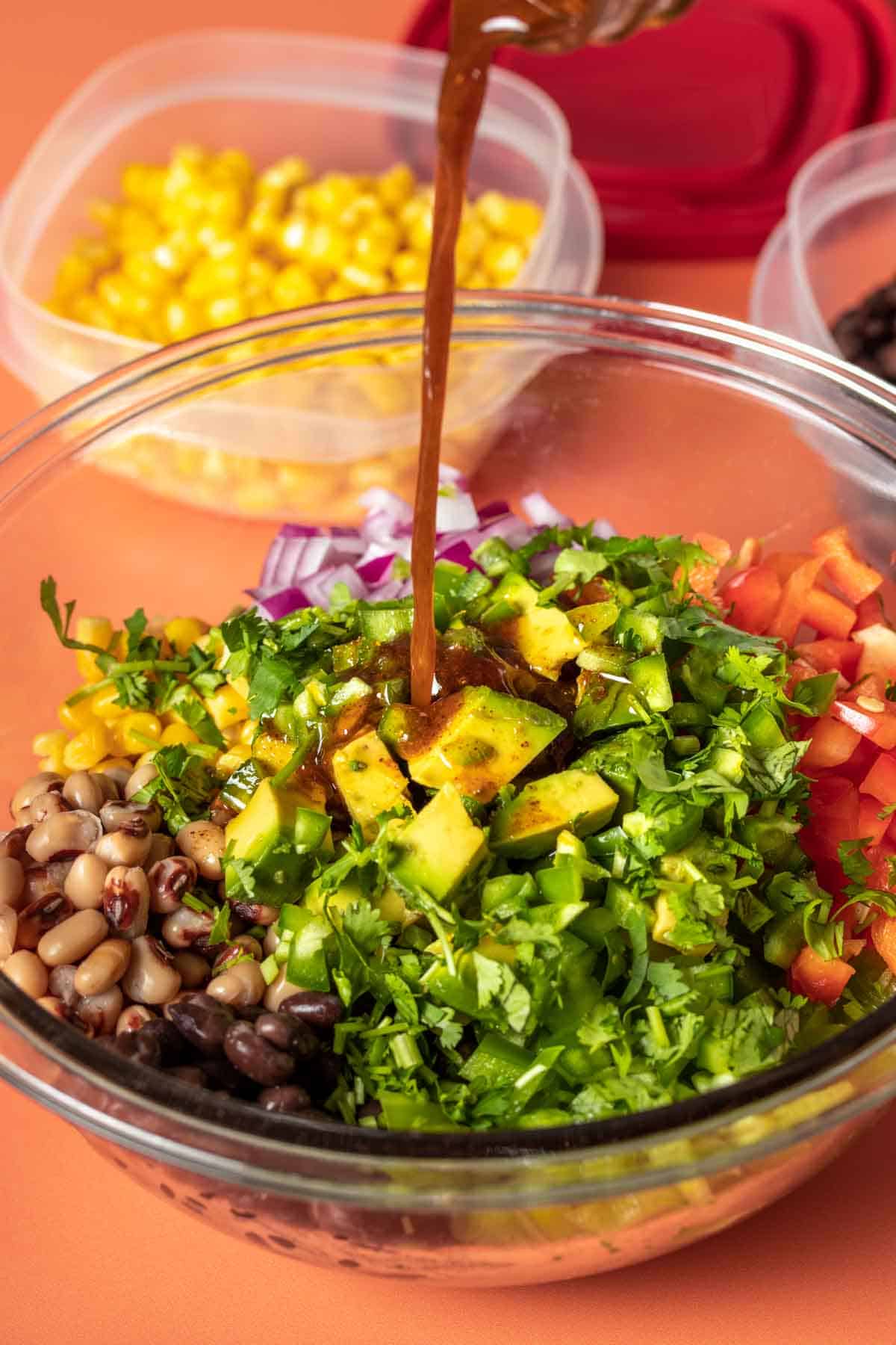 Dressing pouring into a bowl with groups of beans and veggies to make a cowboy caviar.