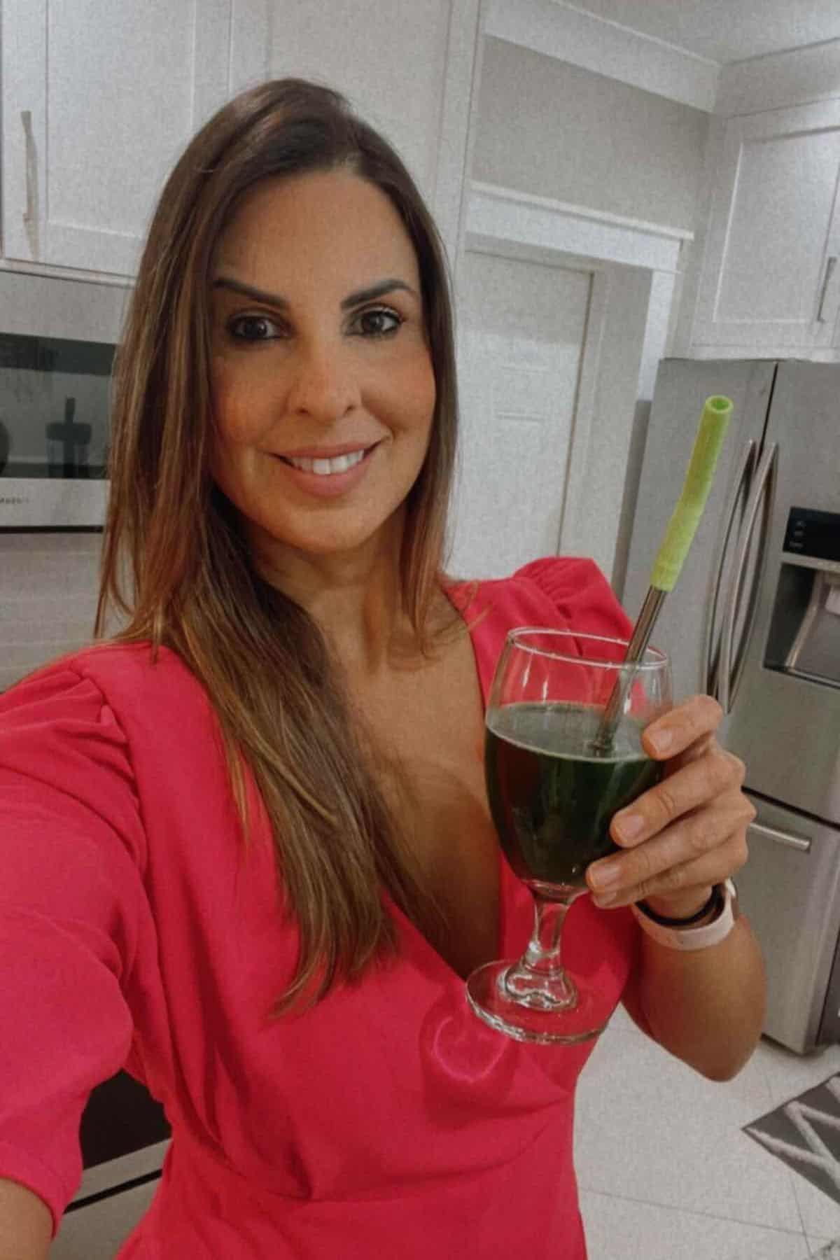 A woman in a red dress holding a glass with green juice and a straw in it.