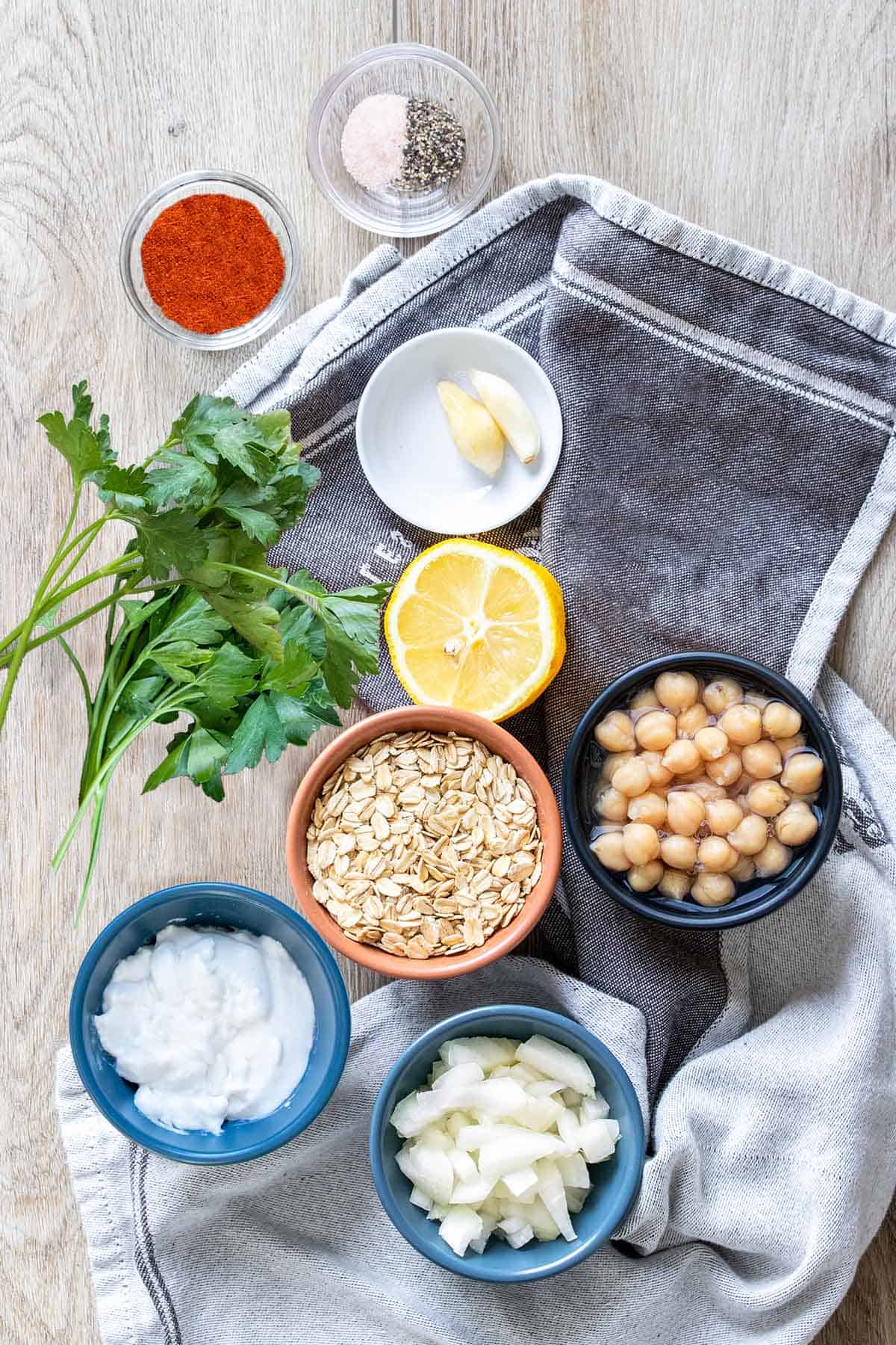 Top view of all the ingredients needed to make a chickpea based veggie burger on a light wood surface.