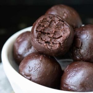 A white bowl with a pile of round brownie bites in it and one on the top has a bite out of it.