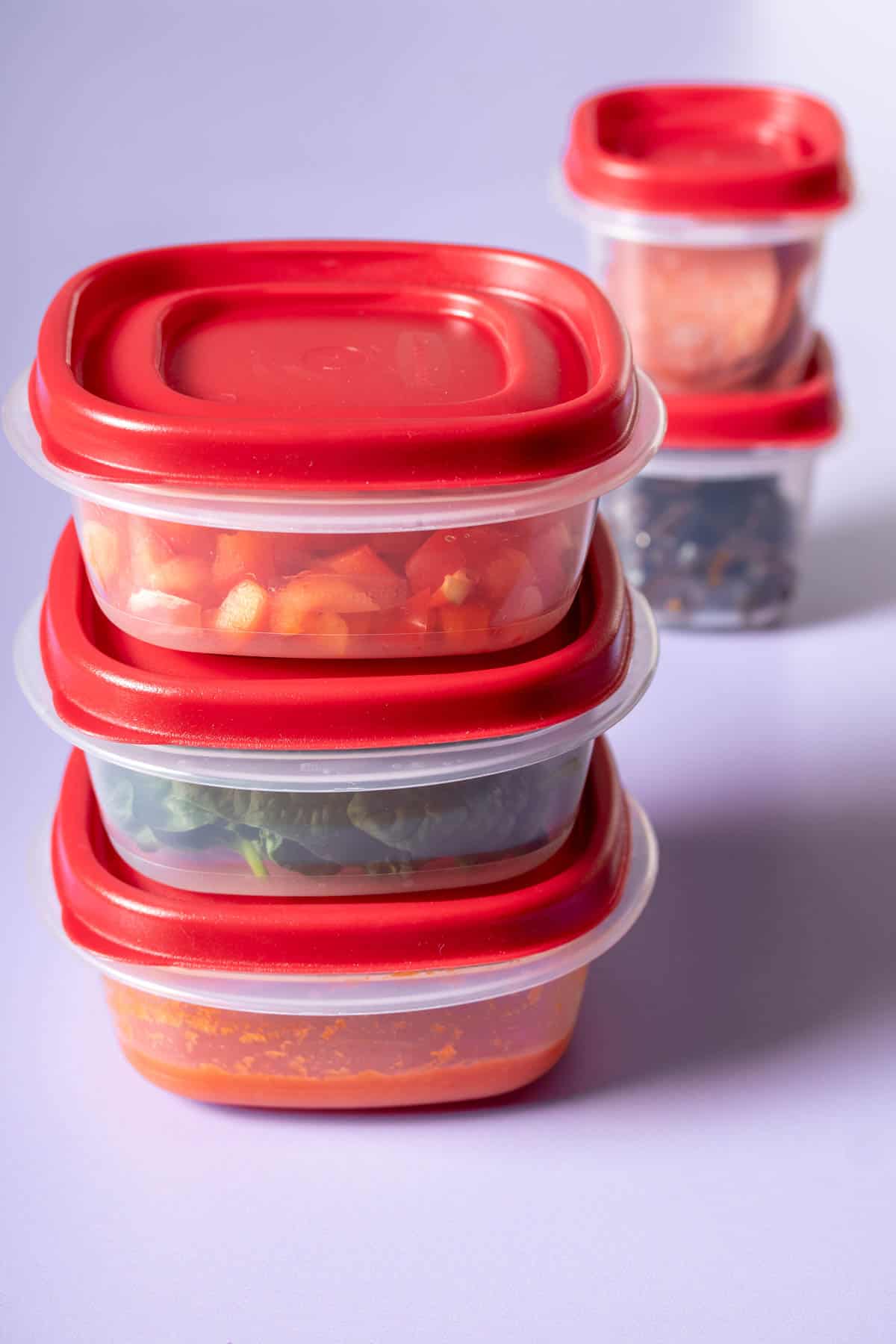A stack of large plastic containers with sauce and veggies in front of two stacked smaller containers.
