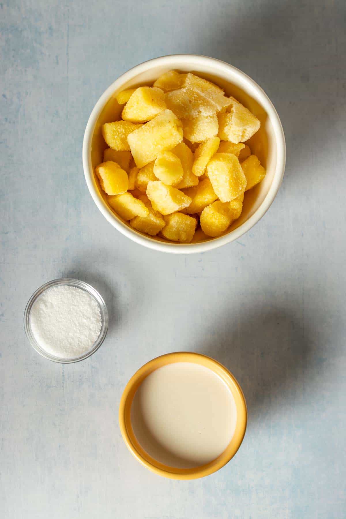 Top view of three bowls filled with frozen pineapple, sugar and milk.