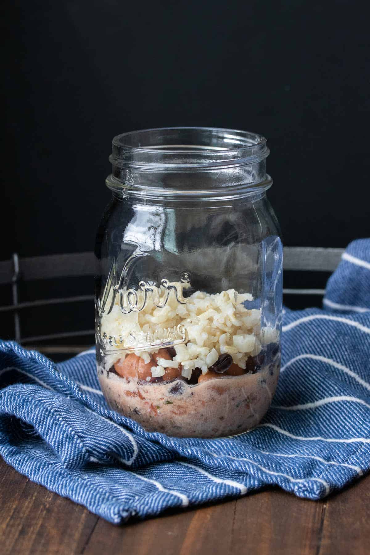 A glass jar on a blue towel with beans and rice in the bottom half of it.